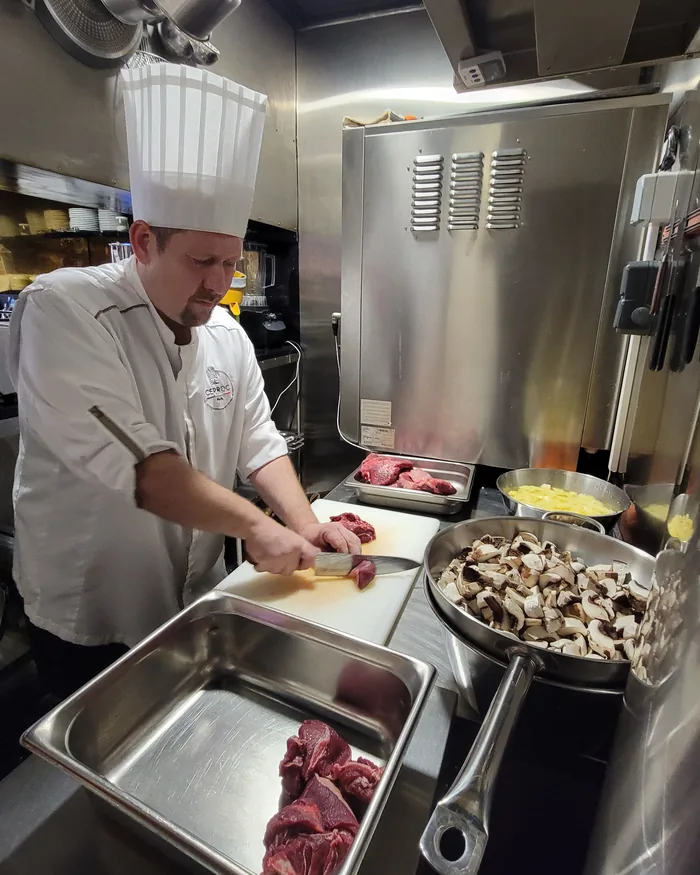 Le chef découpe la viande au couteau dans la cuisine de Pouët-Pouët, restaurant à Pigalle, Paris 9e.