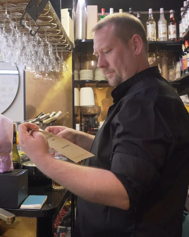 Le chef de Pouët-Pouët derrière le comptoir du bar, la carte du restaurant à la main