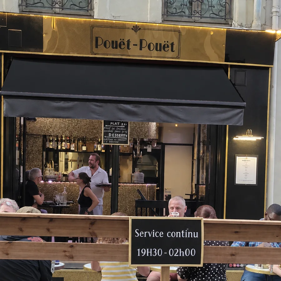 Façade et terrasse du restaurant Pouët-Pouët à Pigalle, avec l'ardoise indiquant les horaires d'ouverture
